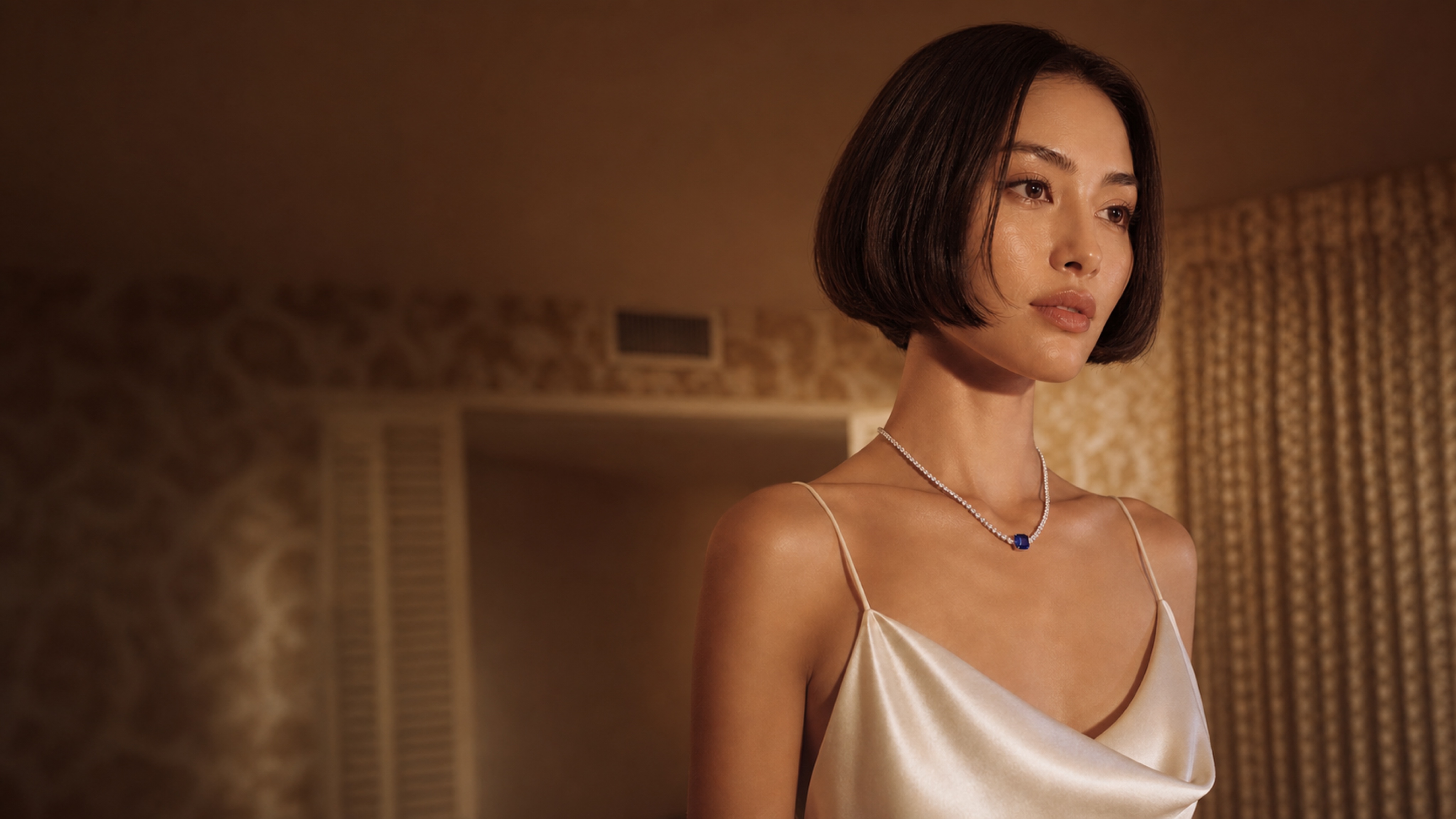 A woman wearing a sapphire pendant necklace in warm editorial light